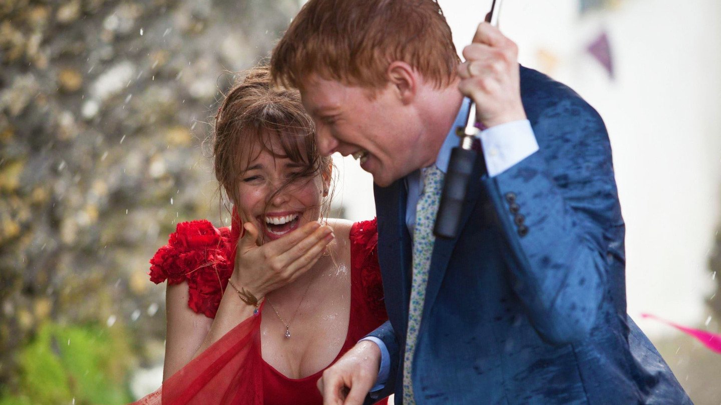 Homem e mulher sorrindo enquanto dividem guarda chuva / Cena do filme Questão de Tempo