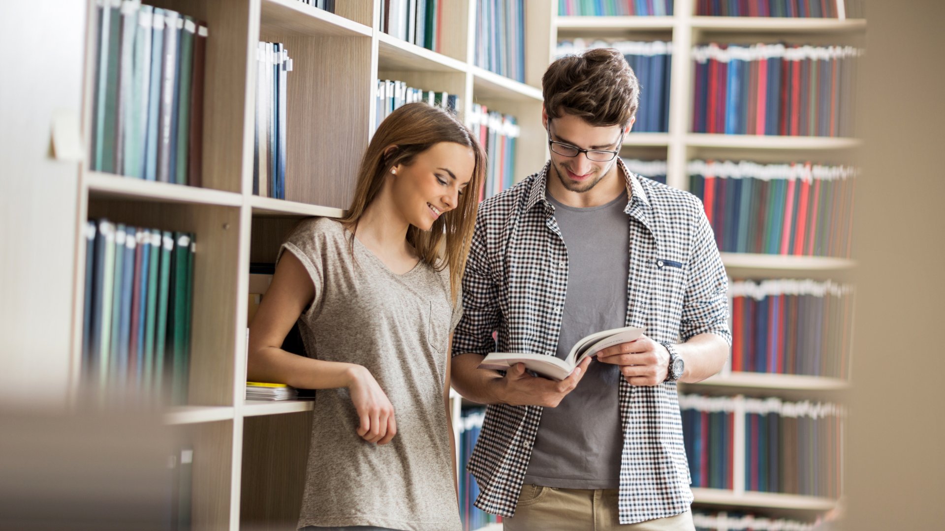 Casal sorrindo na biblioteca lendo um livro juntos