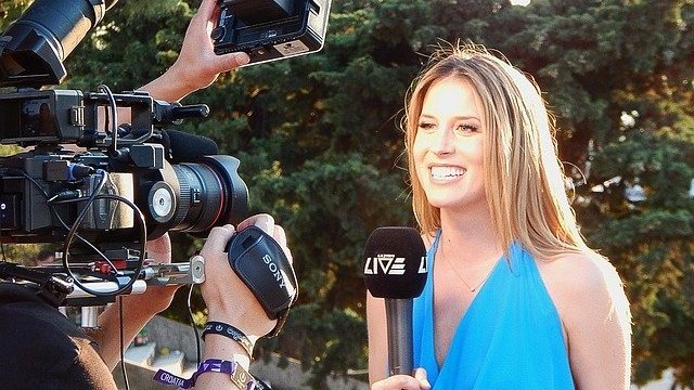 Mulher sorrindo e segurando microfone em frente a câmeras