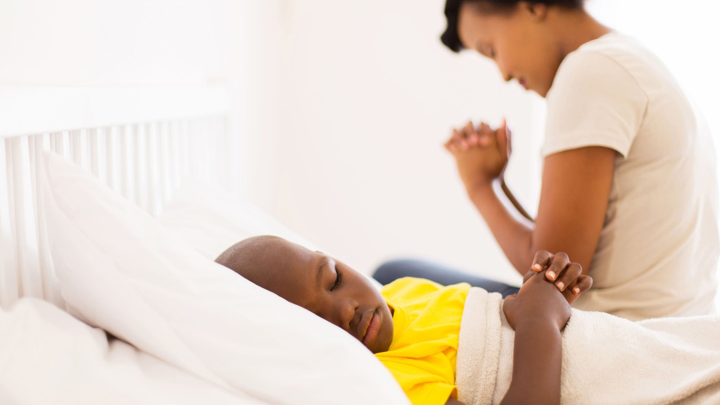 Mãe orando pelo filho que esta deitado dormindo em hospital