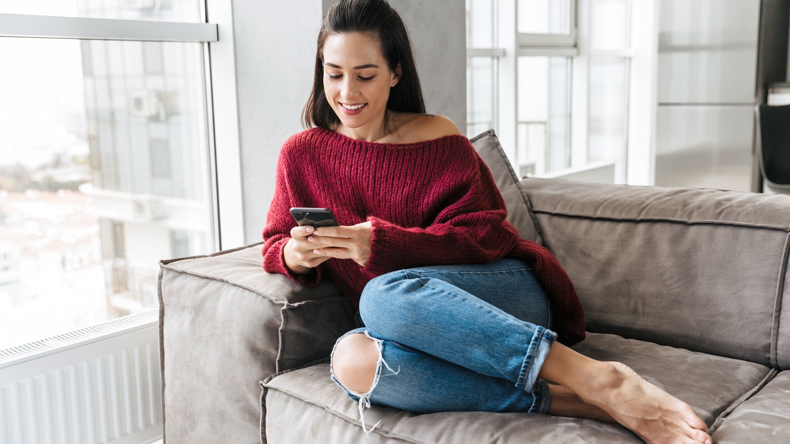 Mulher sentada em sofá digitando em celular sorrindo