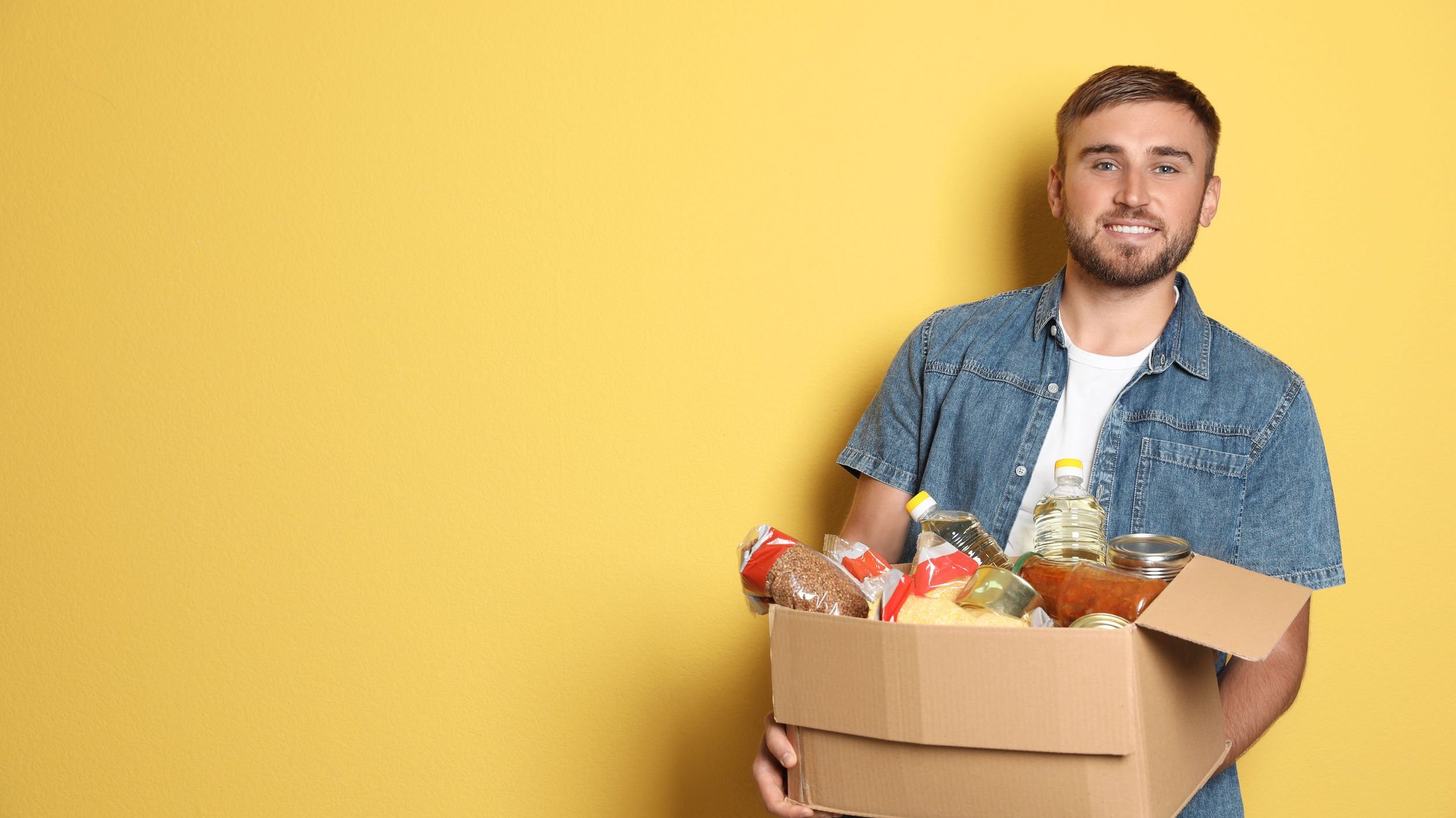 Homem sorrindo, segurando caixa com alimentos.