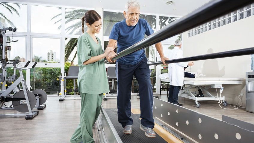 Fisioterapeuta ajudando idoso a caminhar