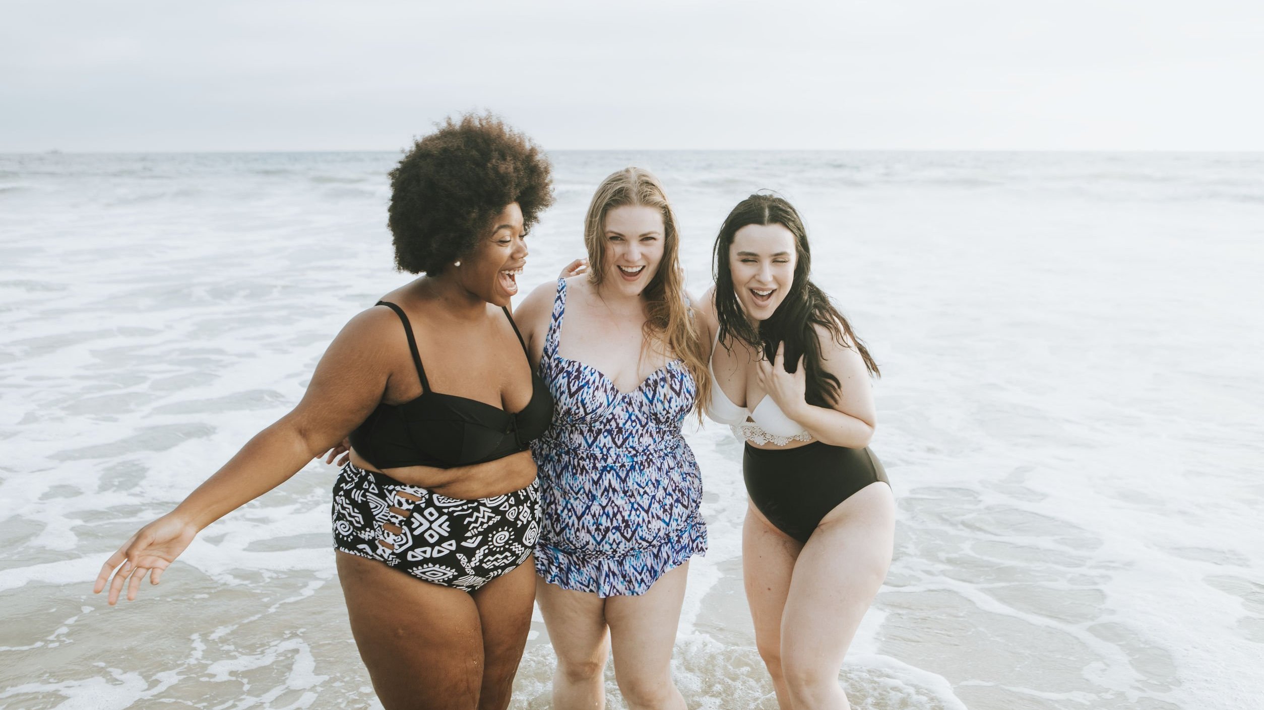 rawpixel - 123RF Mulheres, sendo uma negra e duas negras, na praia com expressões felizes