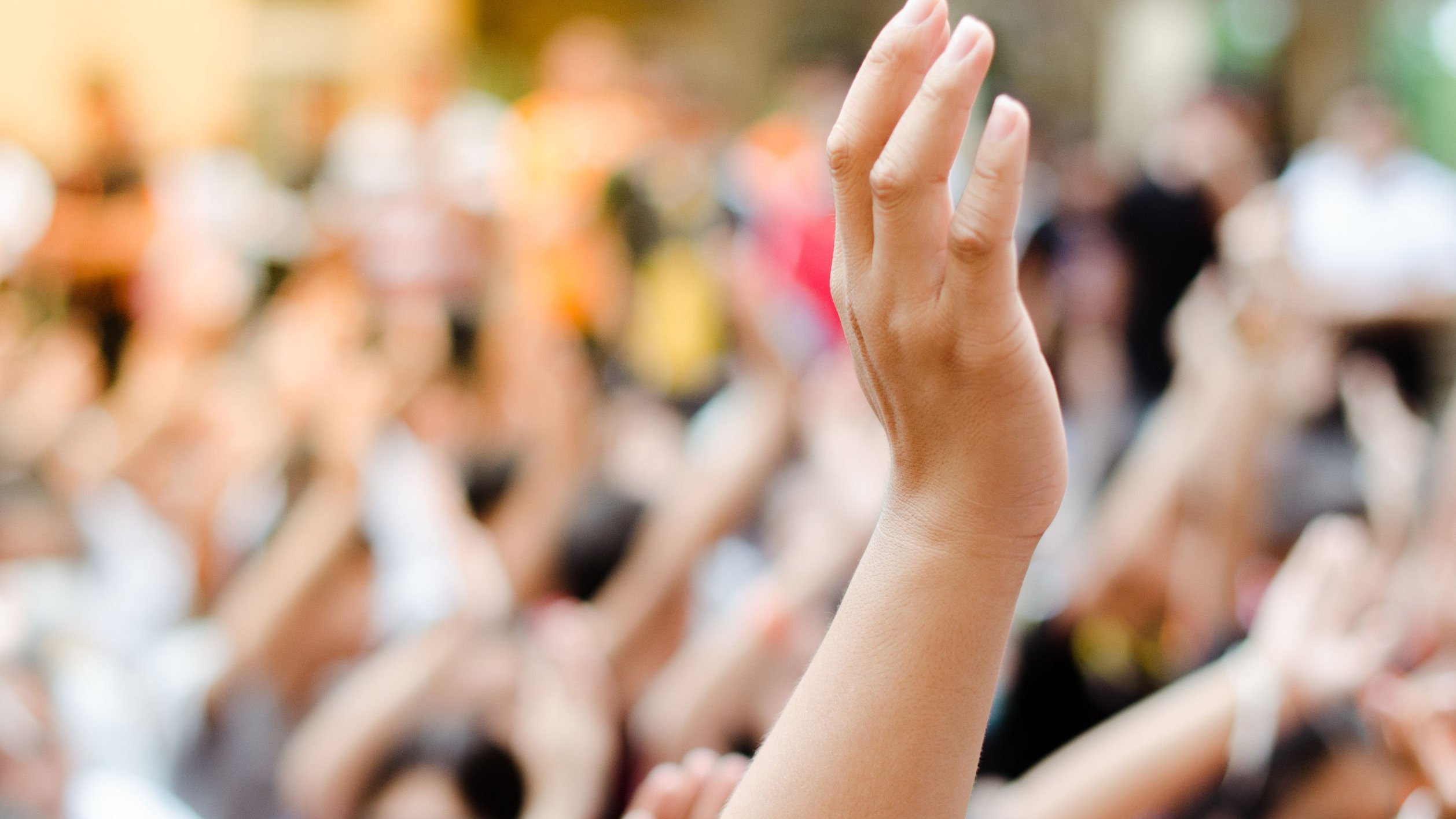 Pessoa levanta sua mão em meio a uma multidão, como forma de demonstrar participação