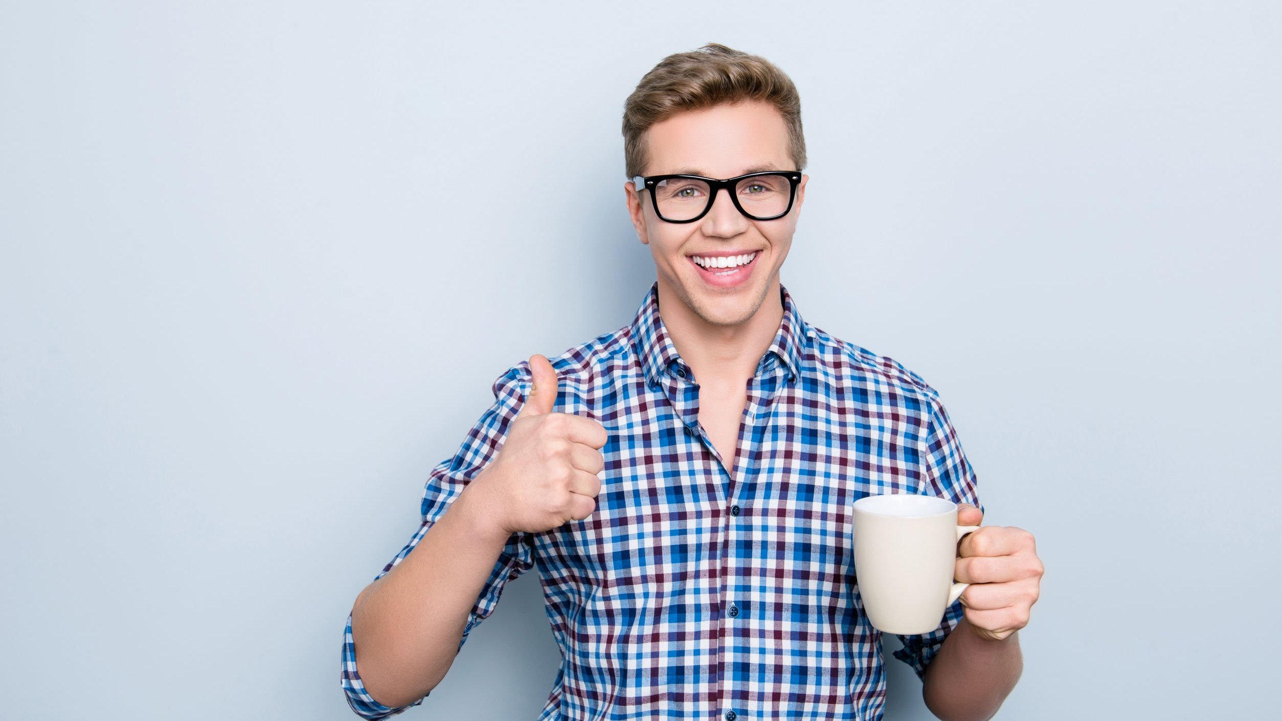 Homem segurando xícara e sorrindo.Fazendo sinal de joia com a mão.