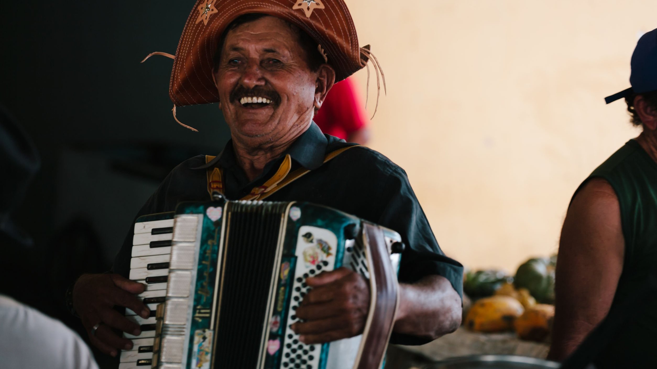 Homem nordestino sorrindo e tocando sanfona.