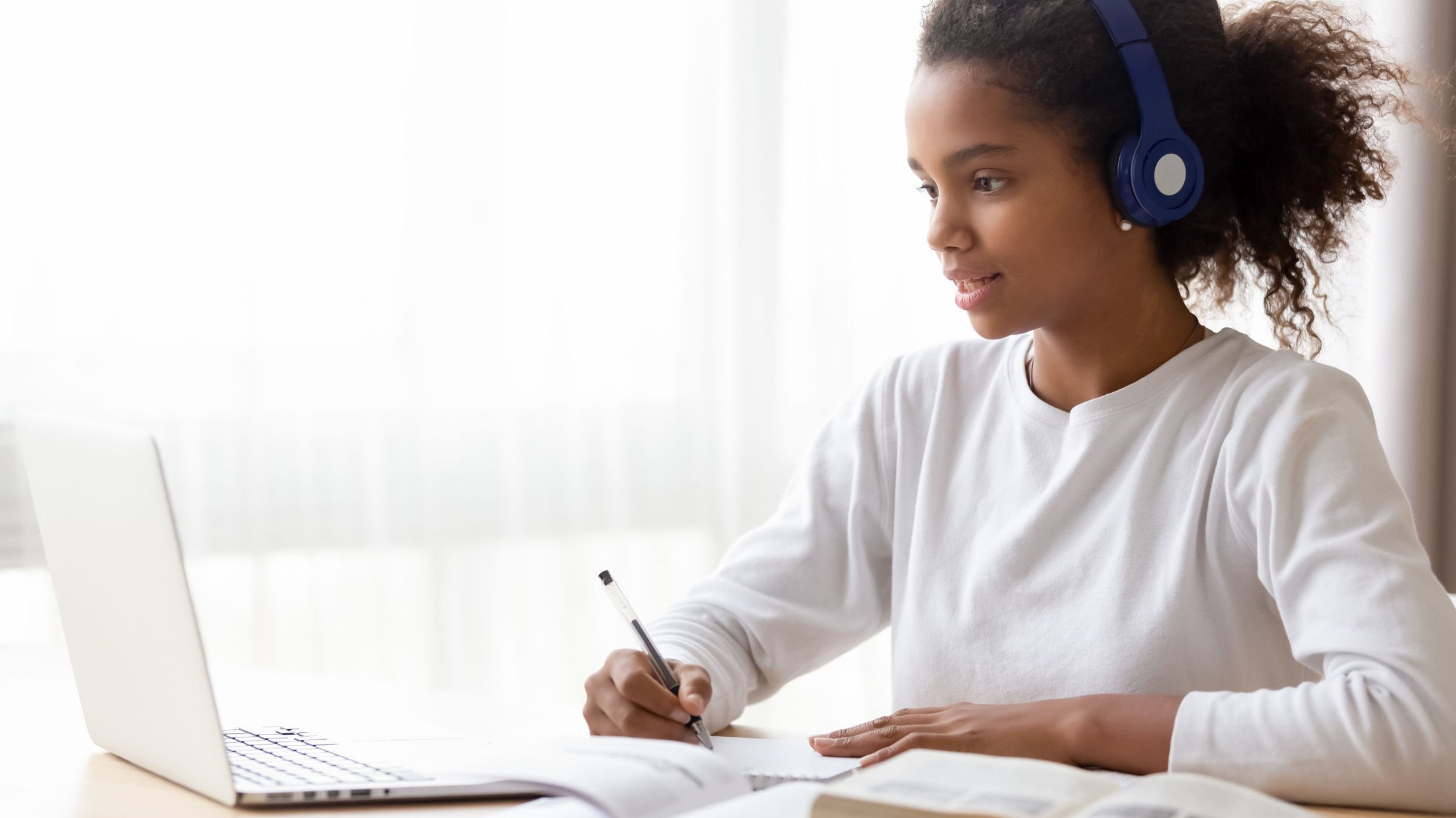 Menina de cabelos cacheados estudando enquanto escuta música em seus fones de ouvido.