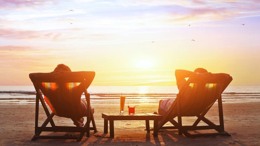 Duas pessoas sentadas em cadeiras de praia olhando pôr-do-sol da areia