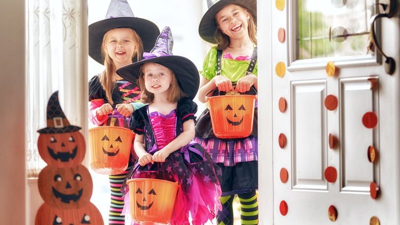 Meninas fantasiadas de bruxas pedindo doces ou travessuras em porta de casa