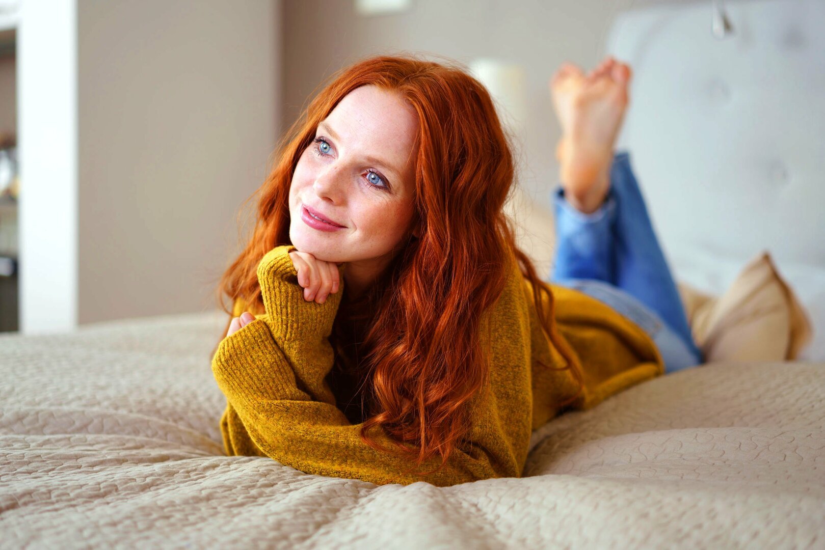 racorn / 123rf Mulher branca e ruiva deitada numa cama com expressão calma e pensativa