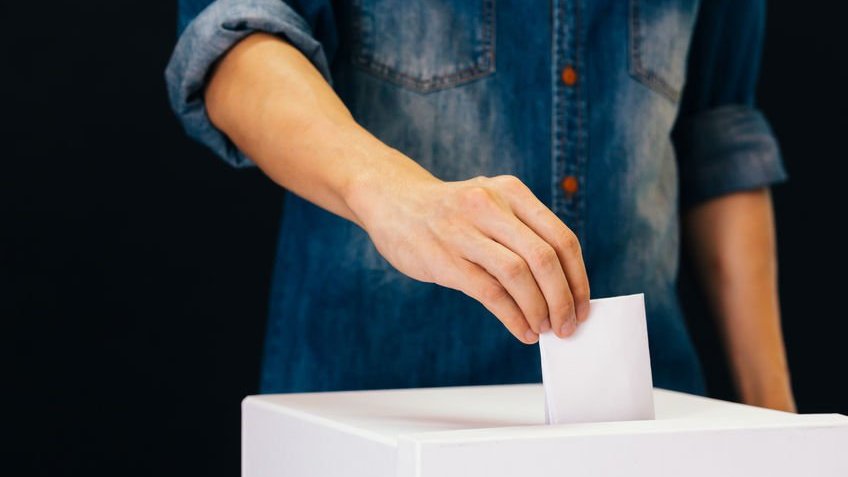 Homem colocando voto em urna de papel