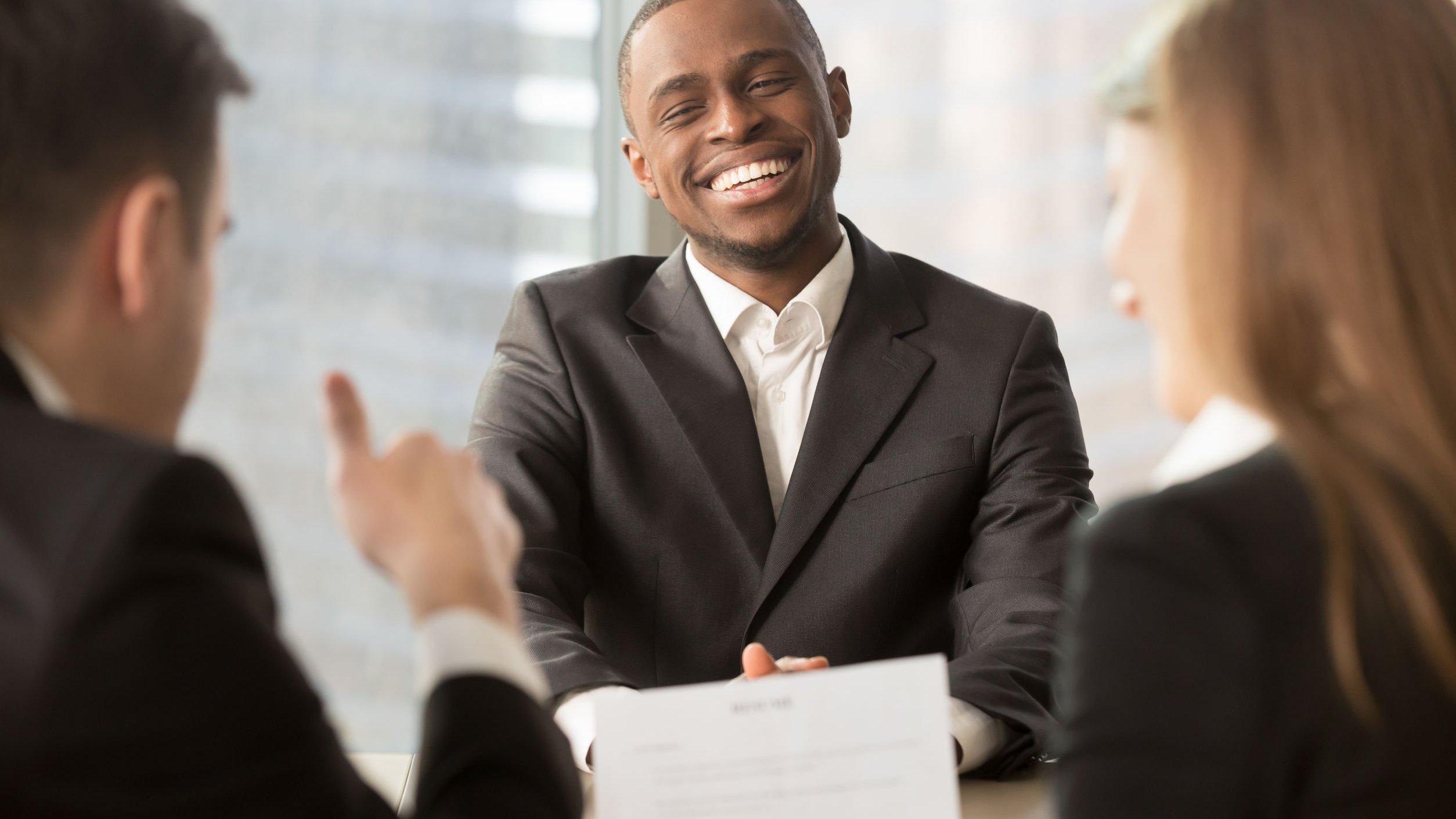 Homem sorrindo no trabalho enquanto cumprimenta duas pessoas.