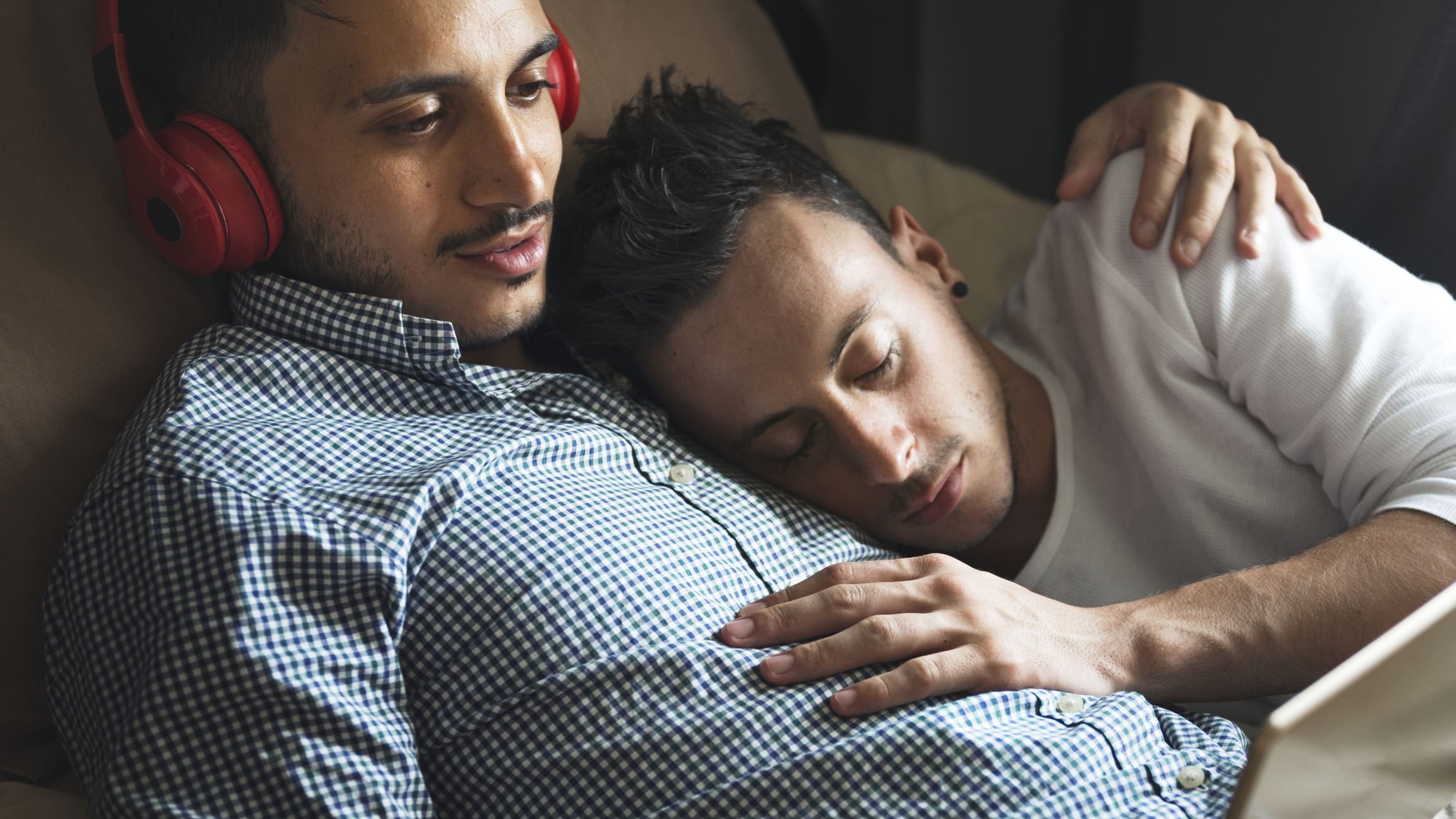 Dois homens deitados, um deles com fones de ouvido vermelho e outro dormindo.