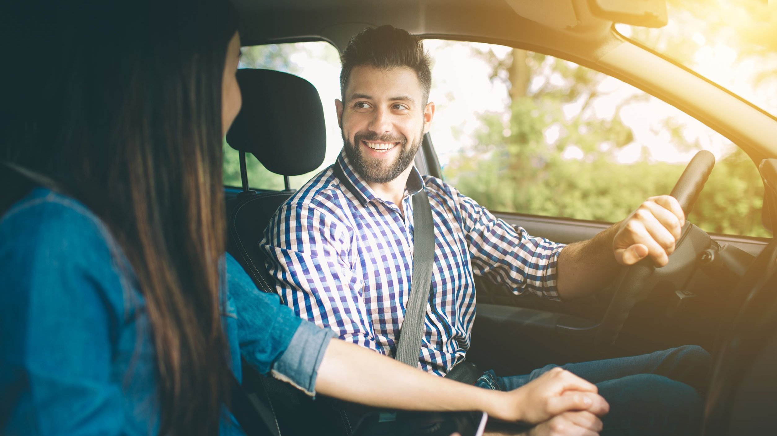 Homem e mulher em carro, sorrindo. Homem usando sinto de segurança.