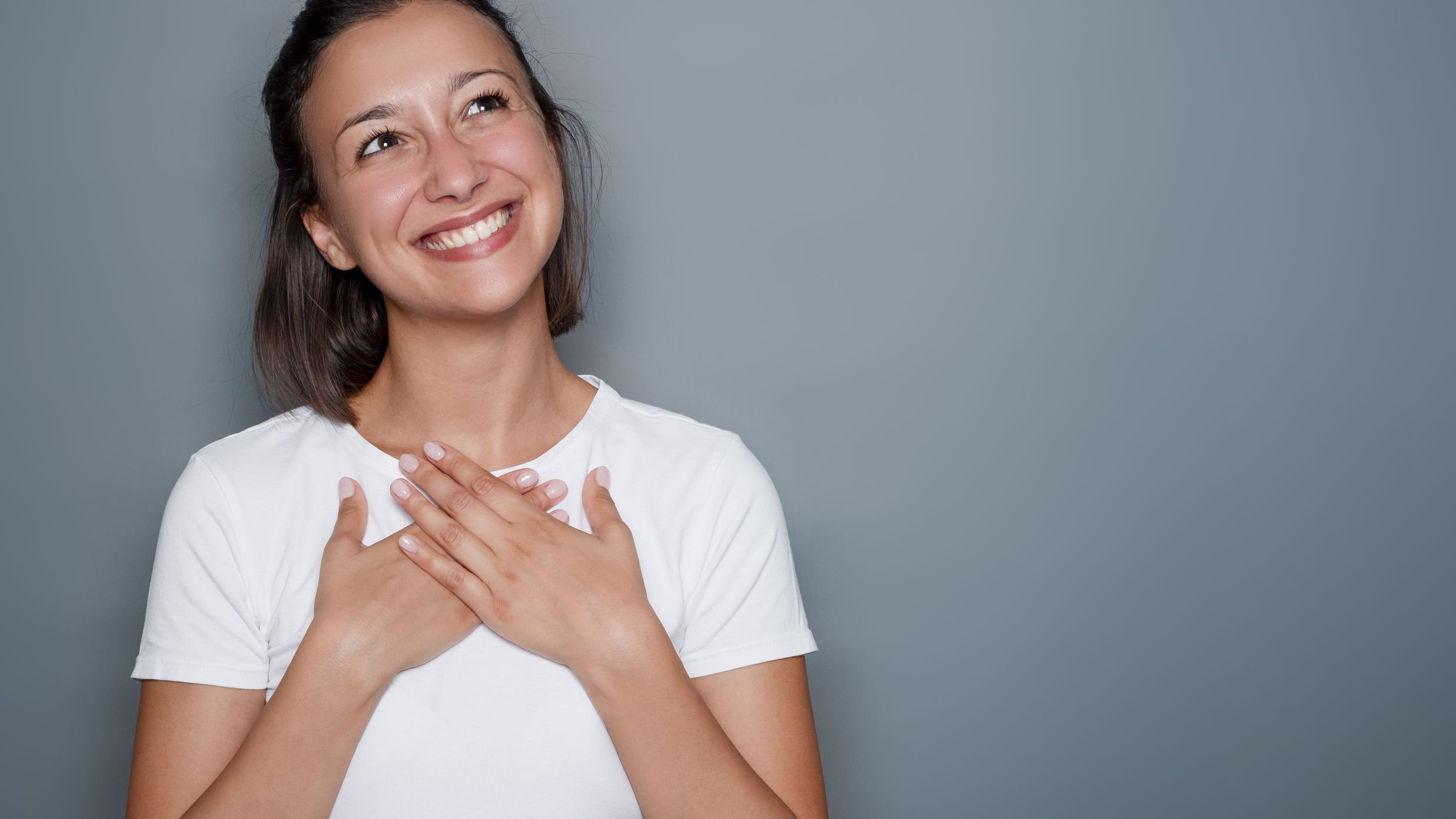 Mulher sorrindo com as mãos no peito.