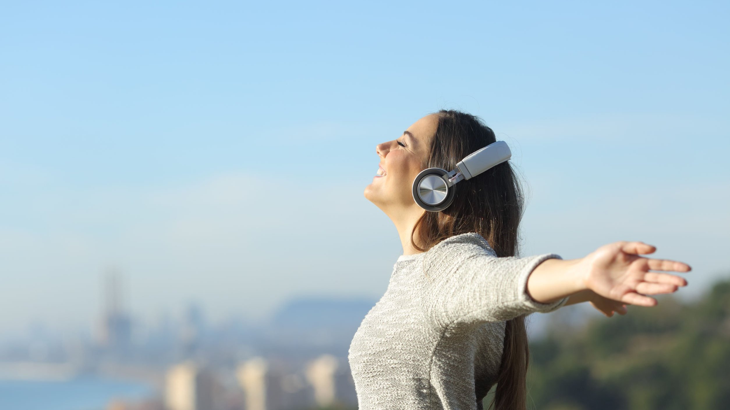 Mulher de braços abertos, sorrindo e com fone de ouvidos, ouvindo música.