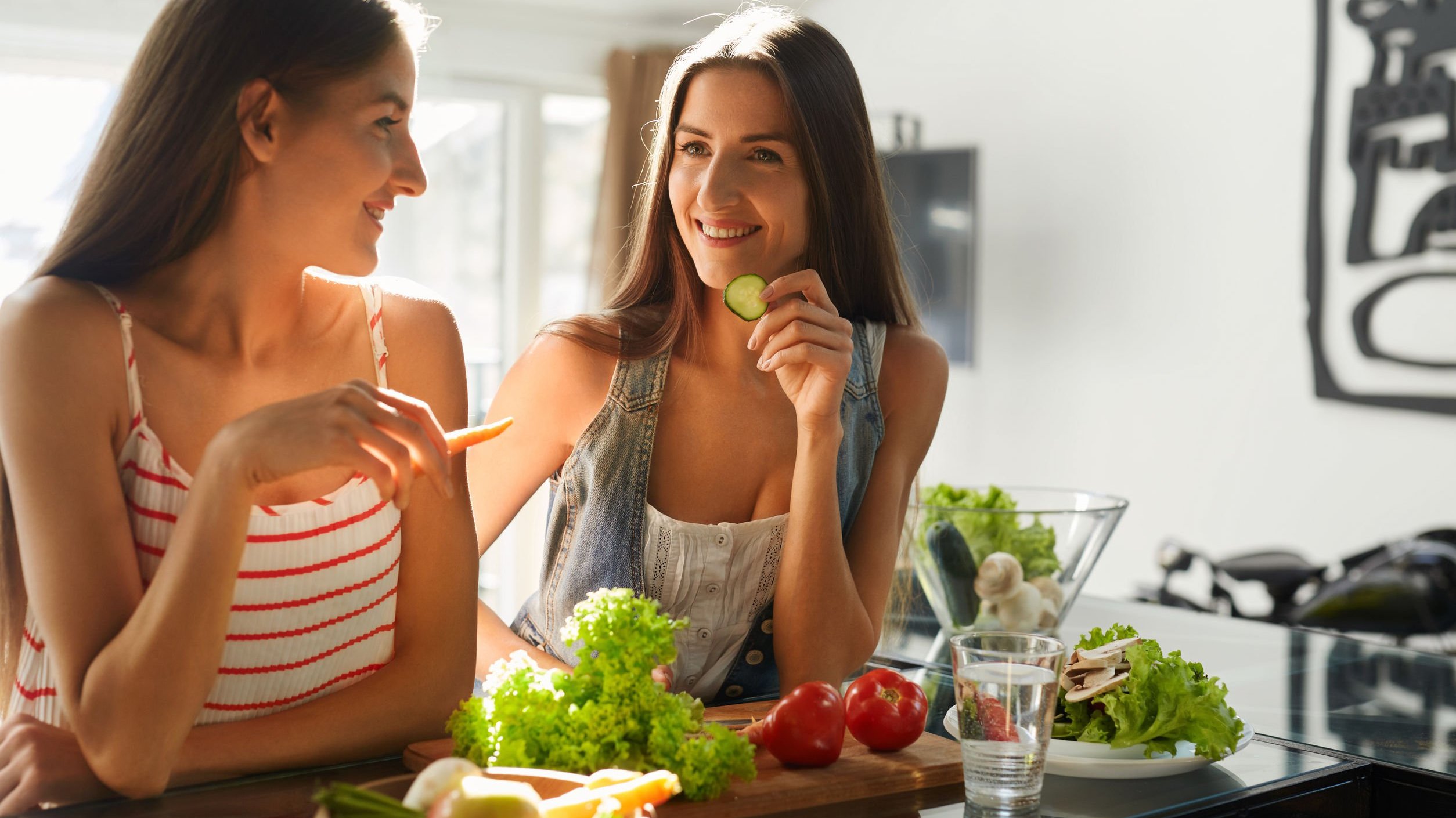 Duas mulheres brancas sentadas num banco comendo vegetais.