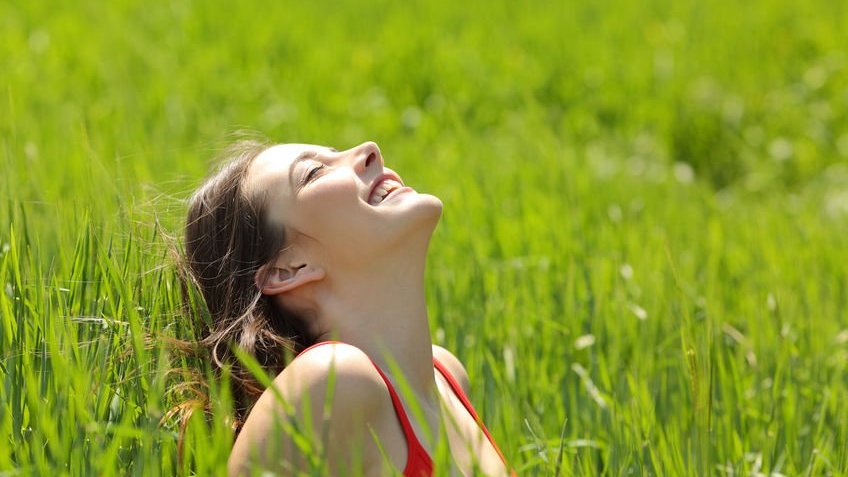 Mulher sentada em gramado alto sorrindo ao sol