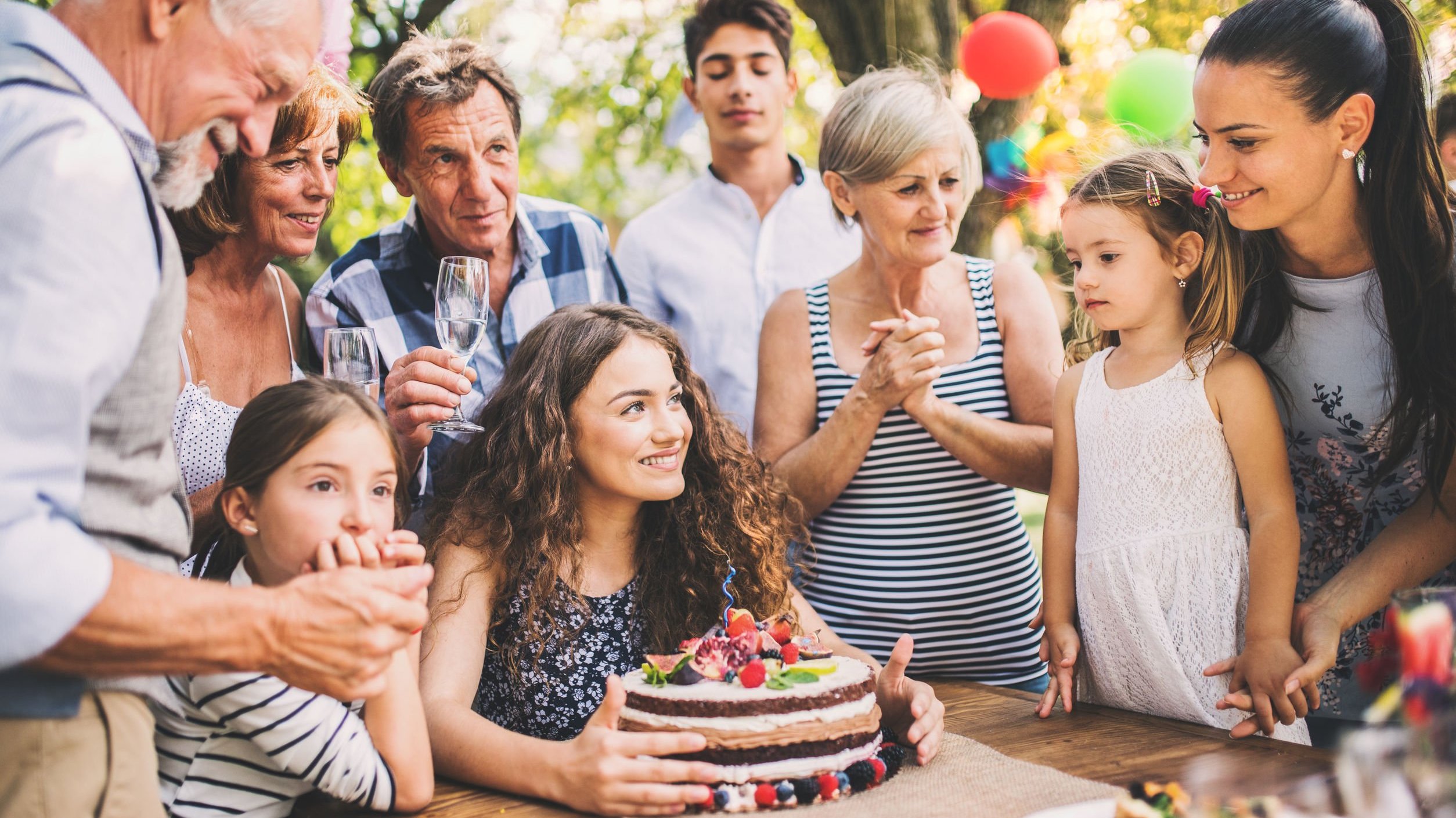 Pessoas comemorando aniversário em volta de menina com bolo
