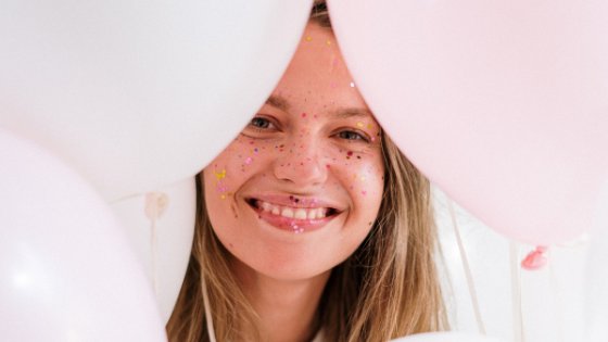 Mulher com Glitter no rosto e com balões de aniversário em volta do rosto