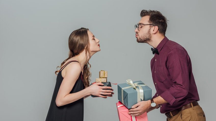 Homem e mulher segurando presentes e fazendo bico de beijo