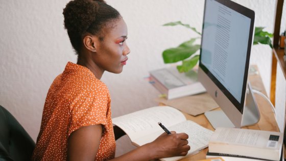 Mulher escrevendo em seu caderno e olhando para o computador