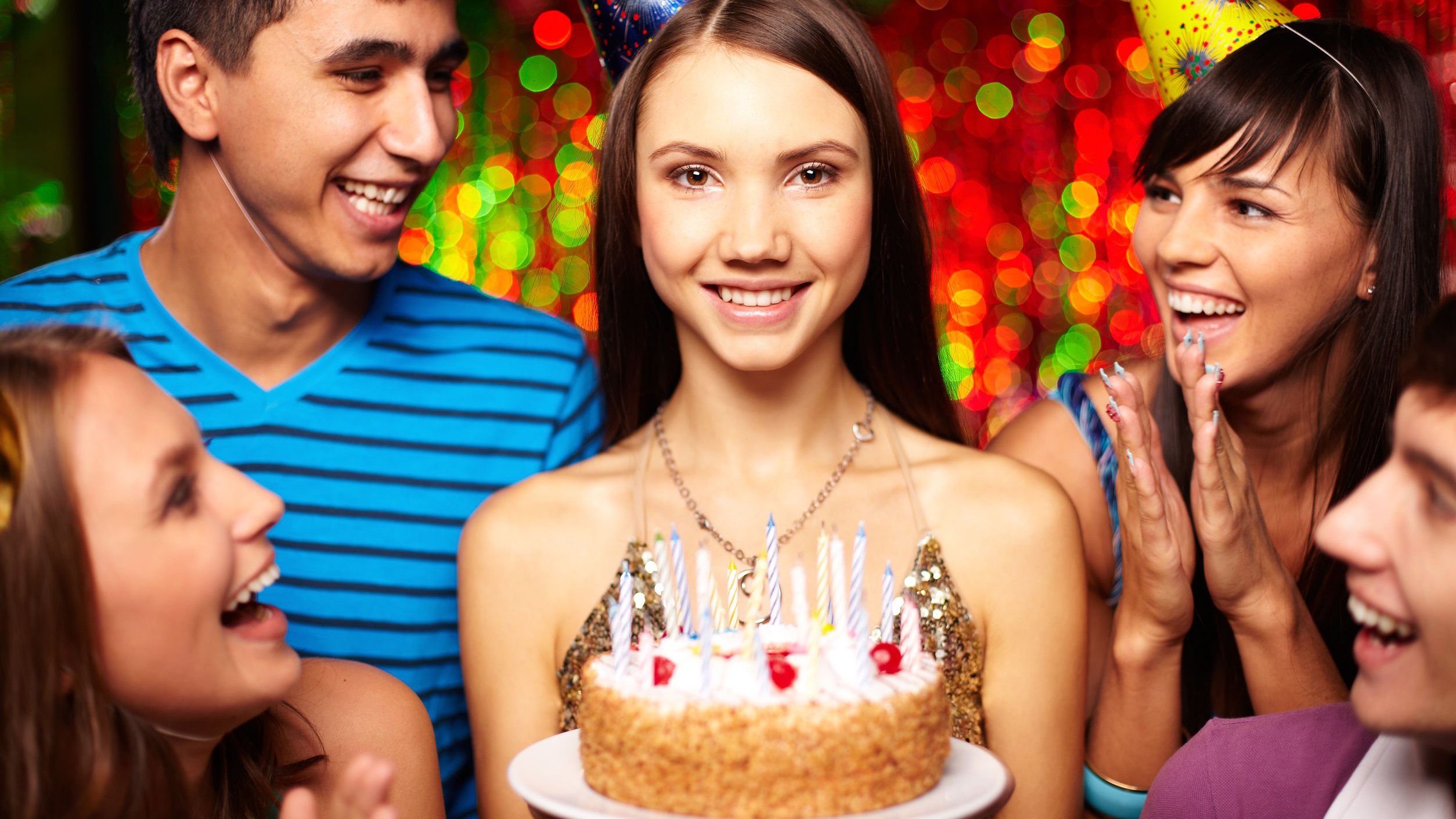 Pessoas comemorando aniversário e mulher sorrindo, segurando bolo.
