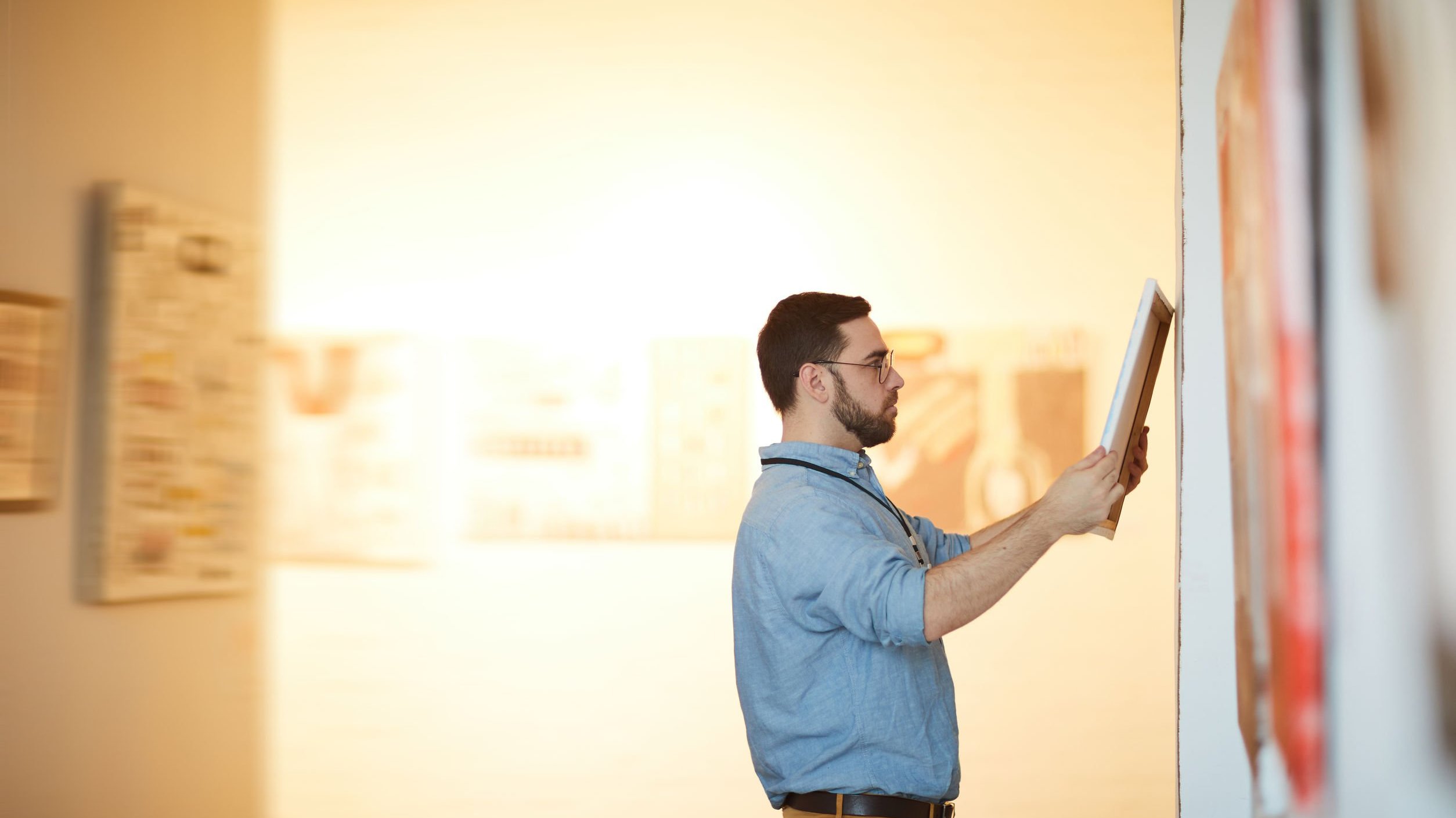 Homem segurando quadro em galeria de arte.