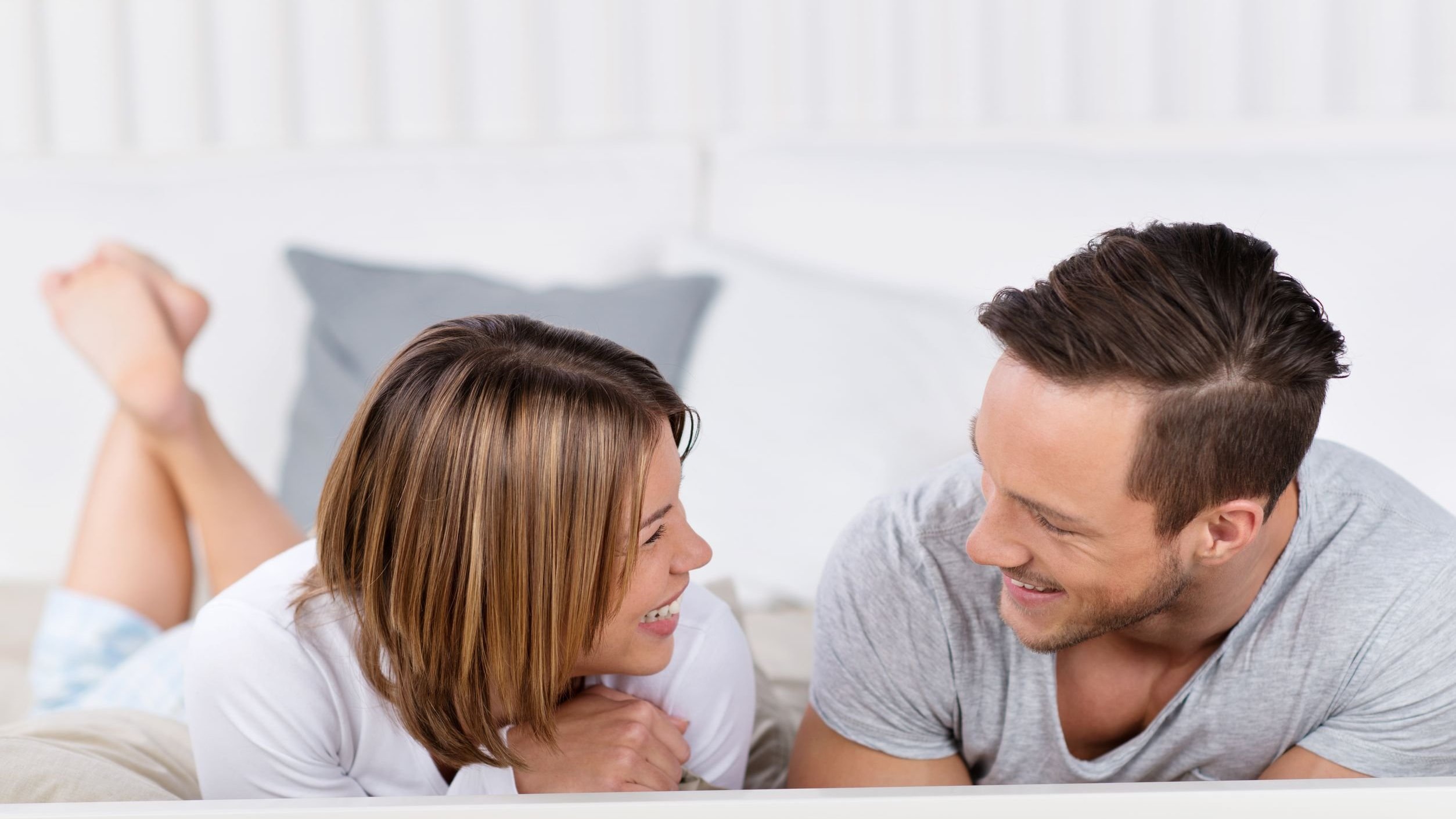 Casal deitado em cama conversando e sorrindo.