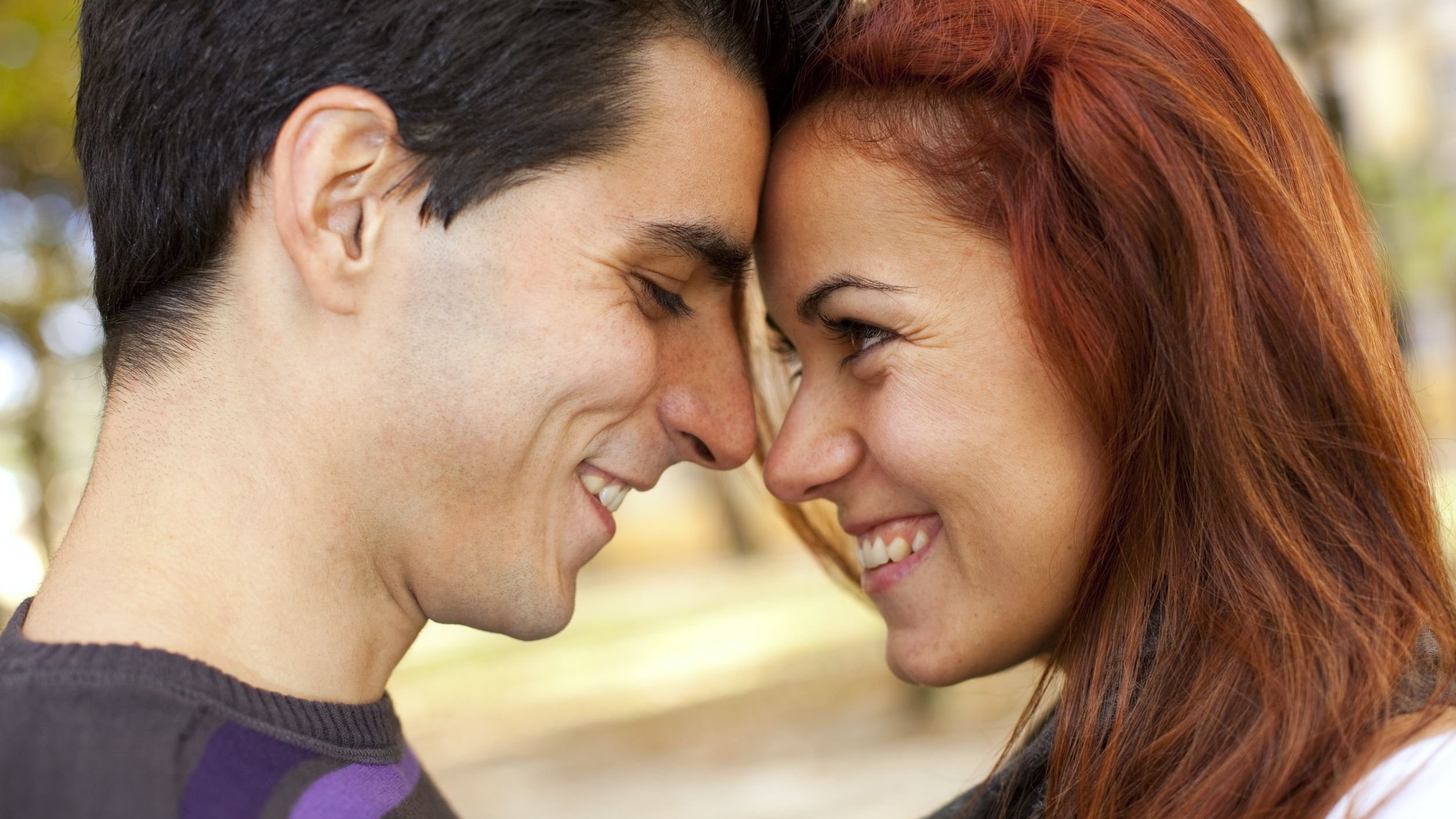 Casal se olhando e sorrindo em parque.