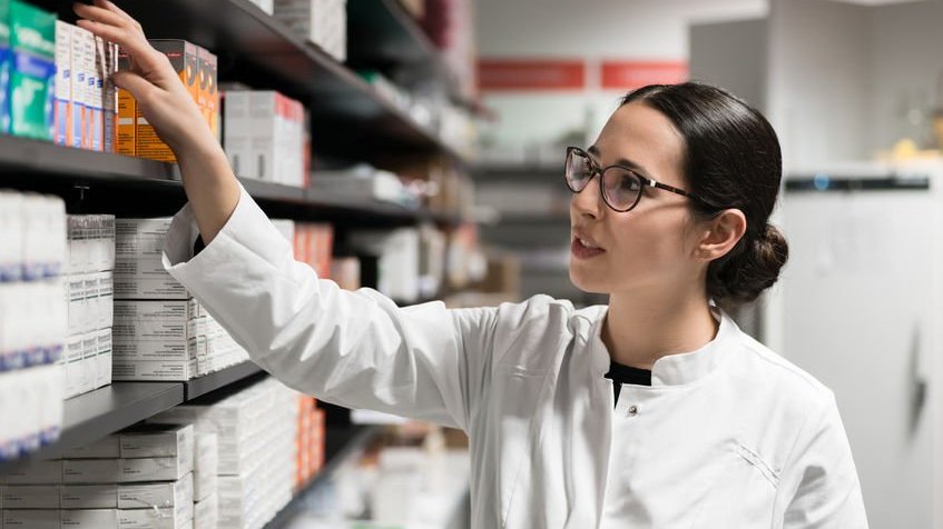 Farmacêutica pegando remédio em prateleira