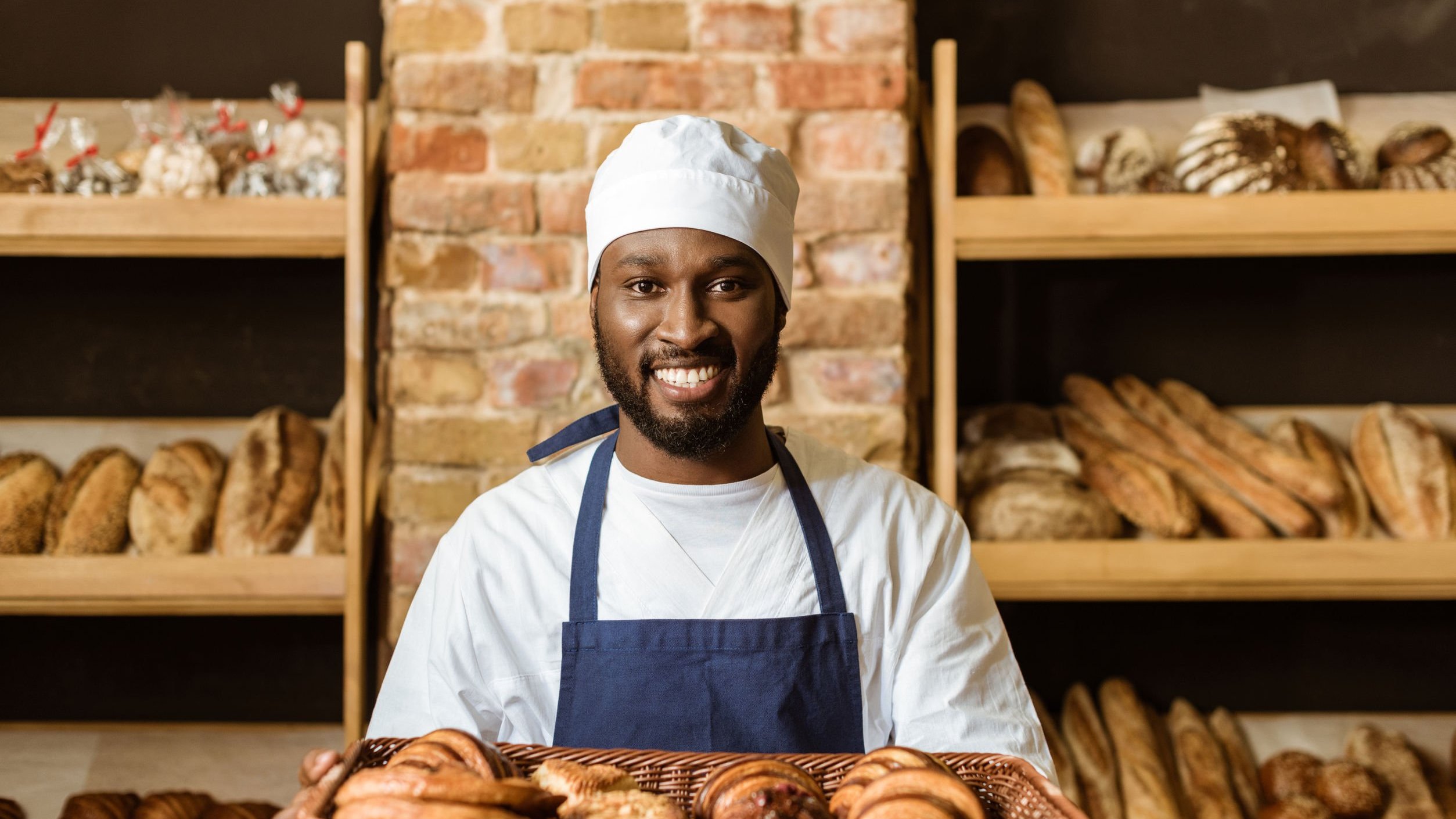 Homem sorrindo segurando bandeja com pães.