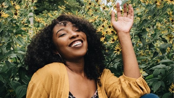 Mulher de olhos fechados sorrindo ao lado de flores