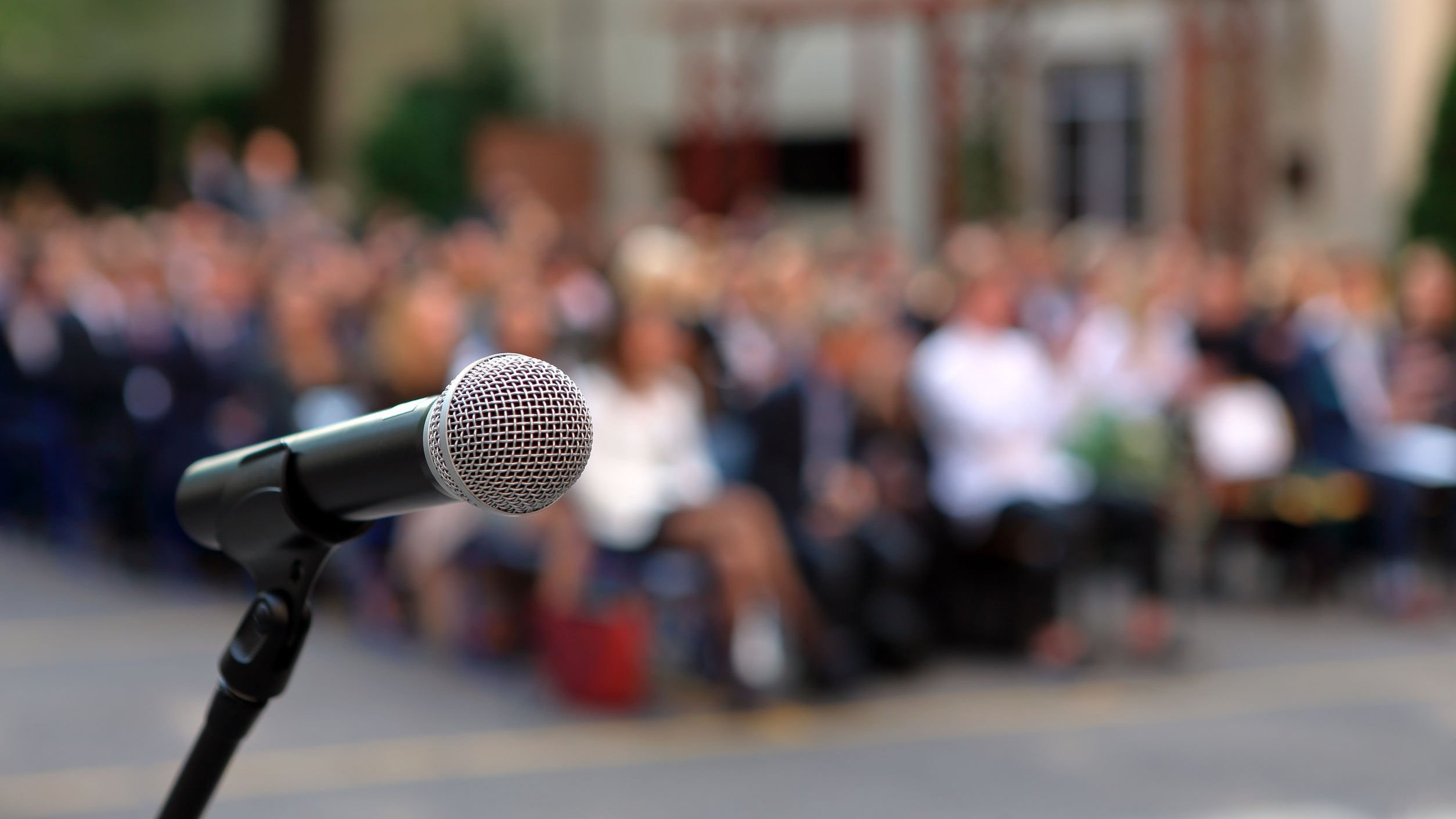 Microfone e plateia ao fundo, aguardando discurso.