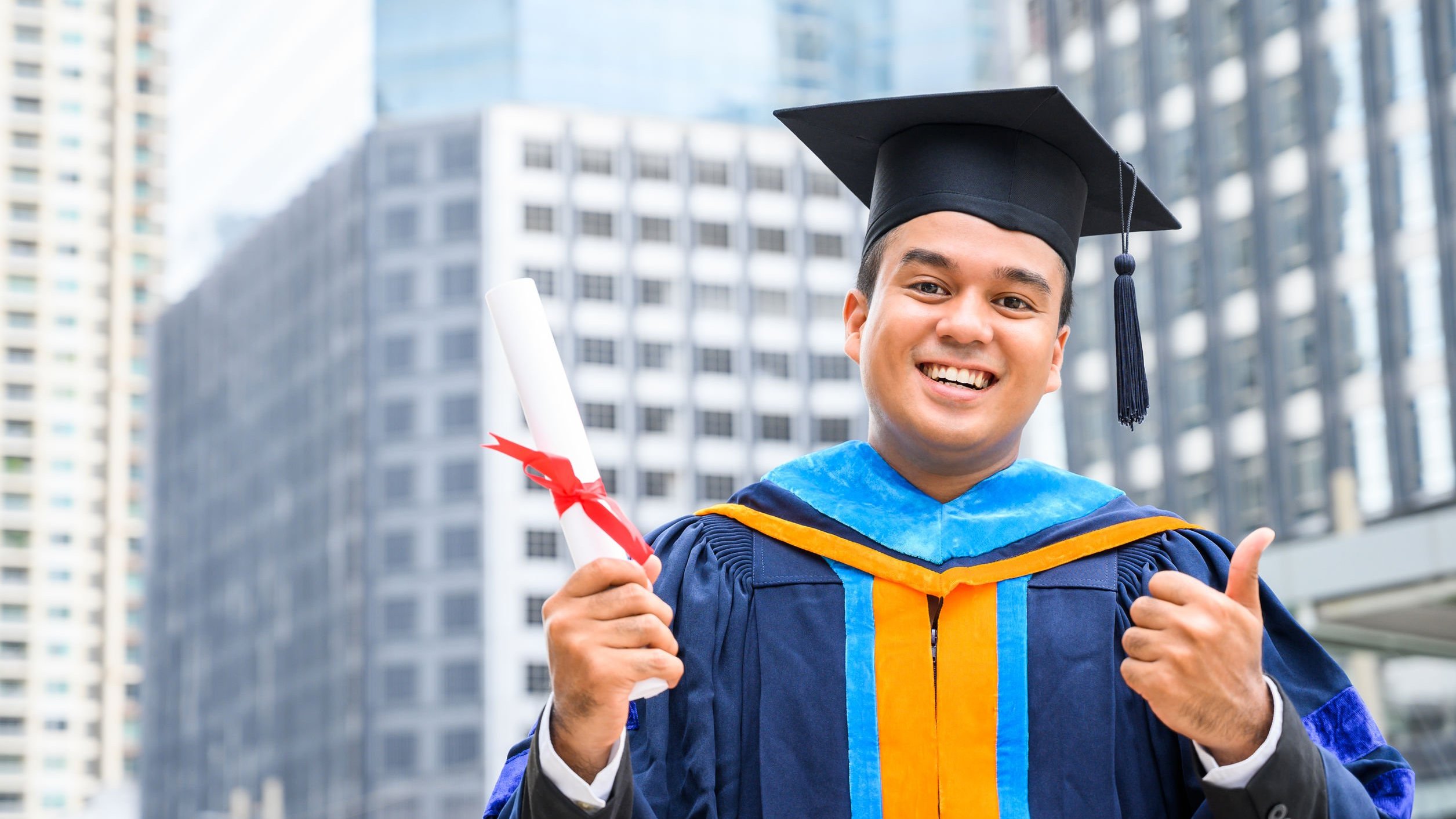 Homem sorrindo, vestido com roupa de formatura, segurando diploma.