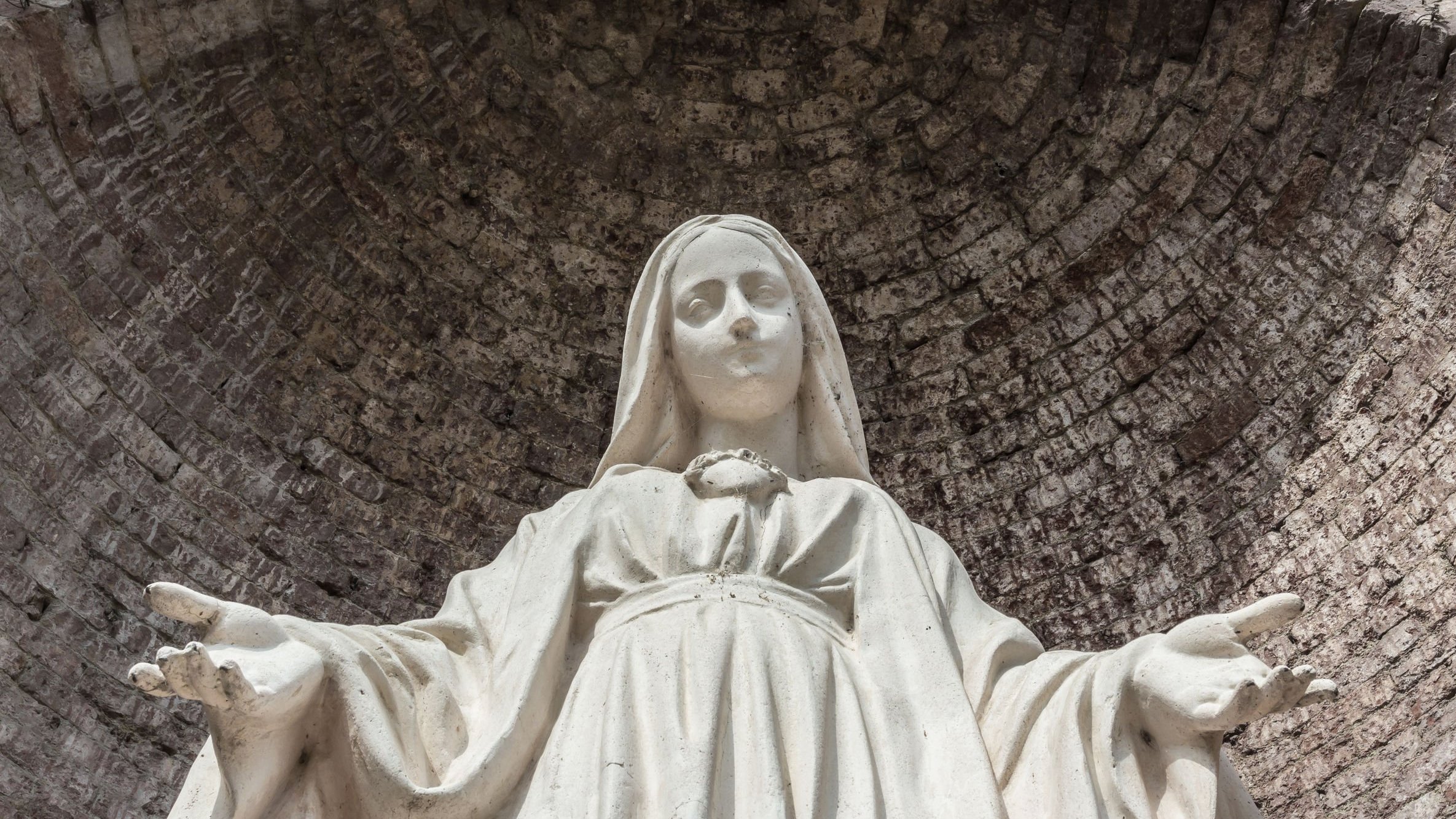 Estátua de Nossa Senhora com os braços abertos, olhando para baixo.