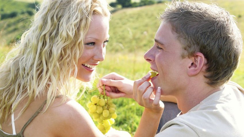 Mulher colocando uva na boca do namorado