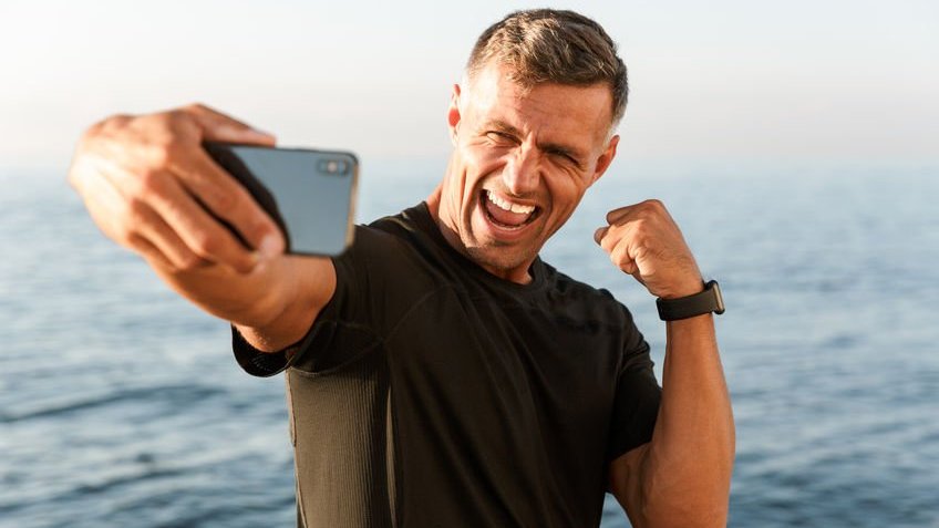 123RF | Dean Drobot Homem tirando selfie sorrindo com mar ao fundo