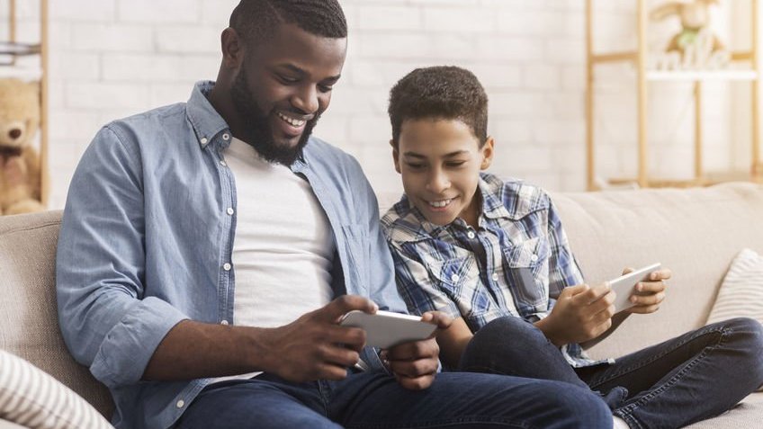 Homem e garoto brincando com eletrônicos no sofá