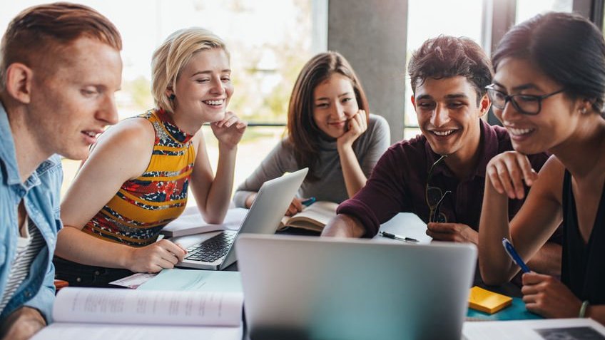 Cinco estudantes sentados olhando para tela do notebook que está à frente