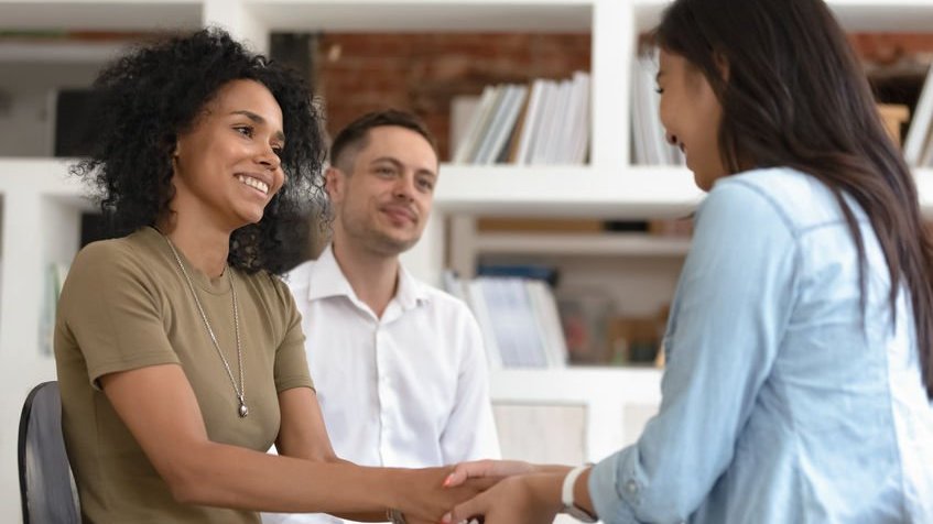 Duas mulheres dando as mãos sorrindo e um homem ao lado delas