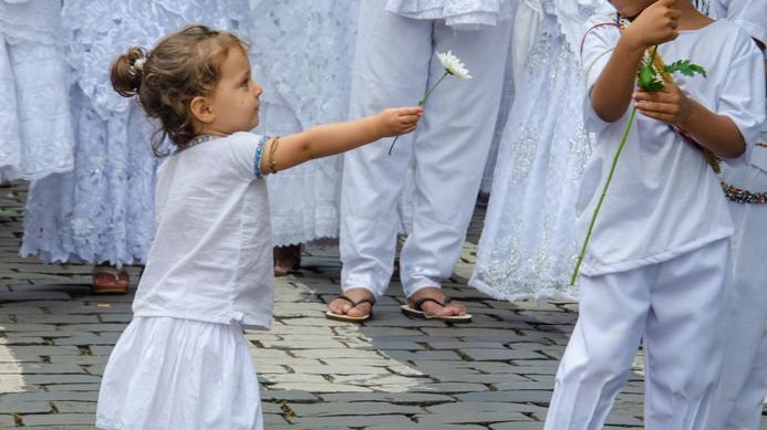 Criança usando trajes da Umbanda oferece flor para outra criança.