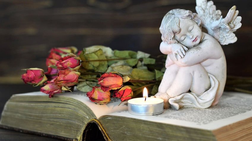 Uma pequena estátua de anjo, vela e rosas secas em cima de uma bíblia