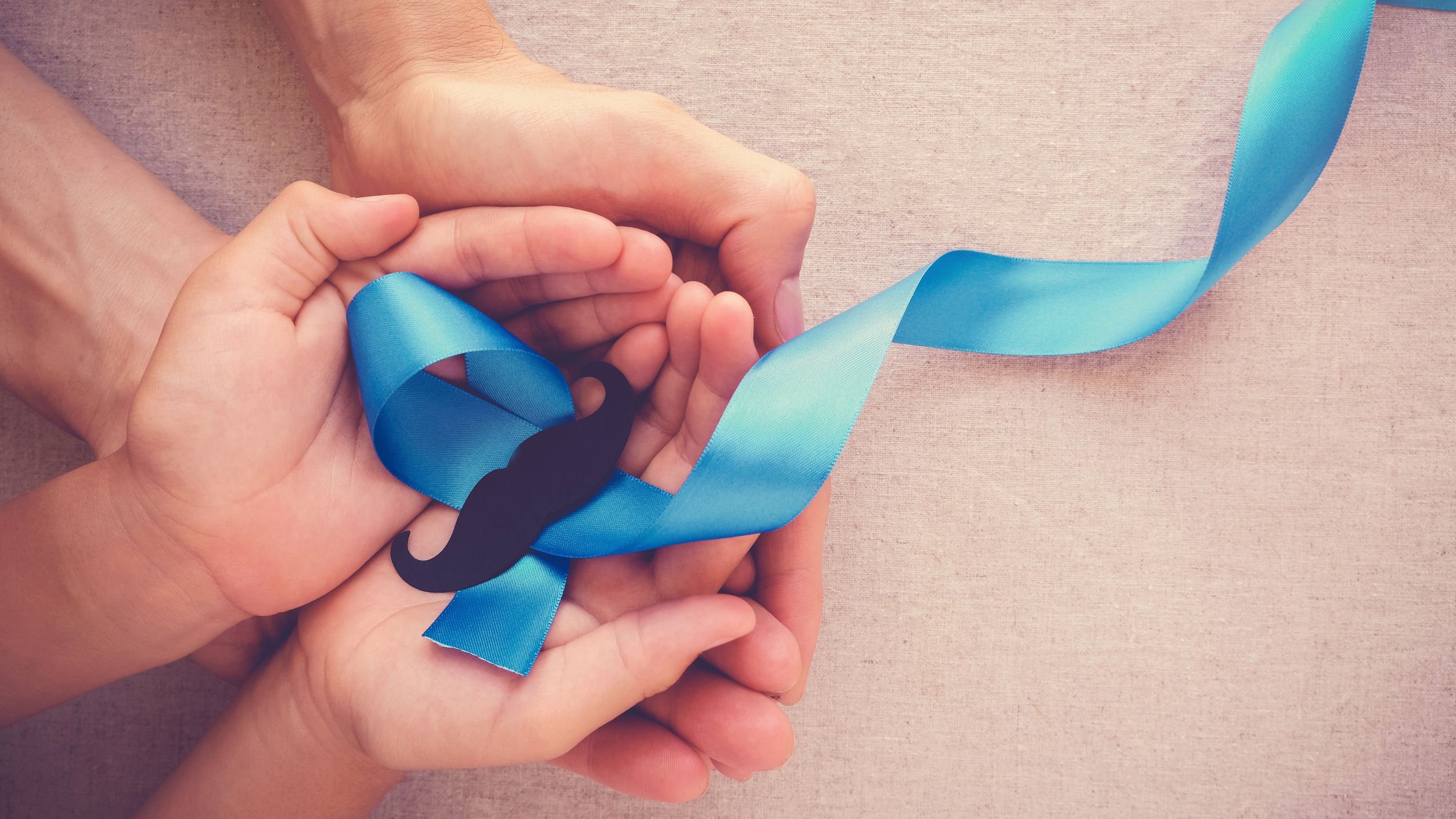 Mãos de uma criança e de um homem adulto segurando um bigode sobre fita azul