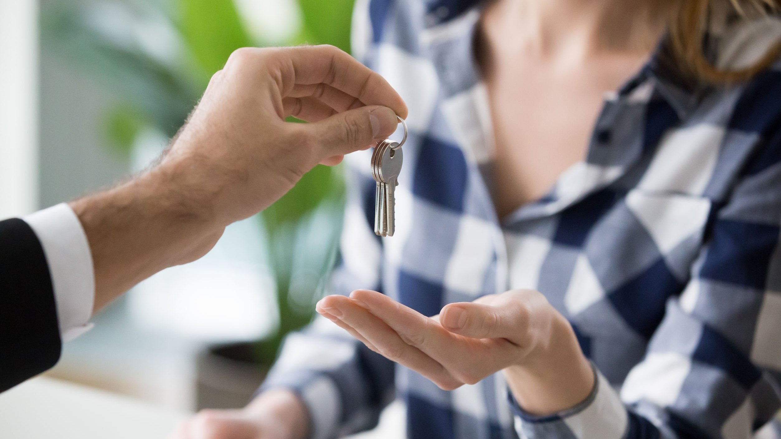 Mão de homem entregando chave de casa para mulher.