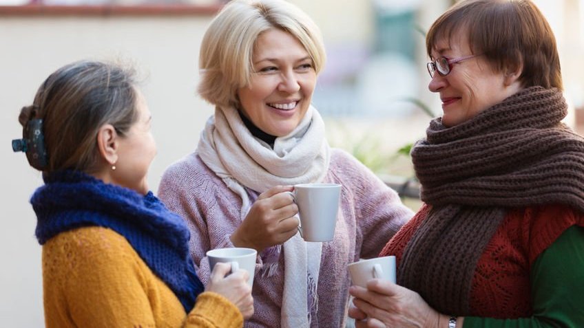 Três amigas de longa data conversam enquanto tomam um café