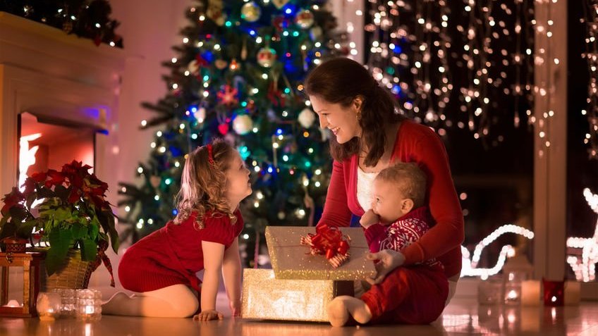 Família na véspera de Natal abrindo presentes de Natal.  Sala com lareira e árvore decorada.