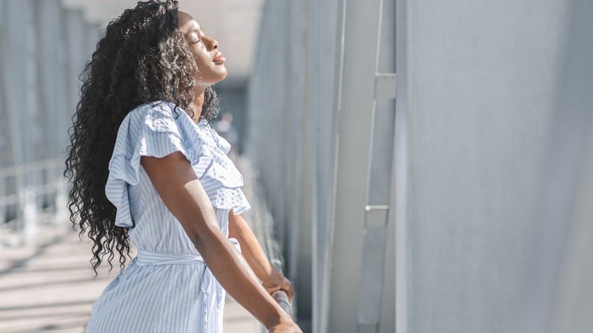 Mulher parada em frente de uma janela sente a luz do sol bater em seu rosto