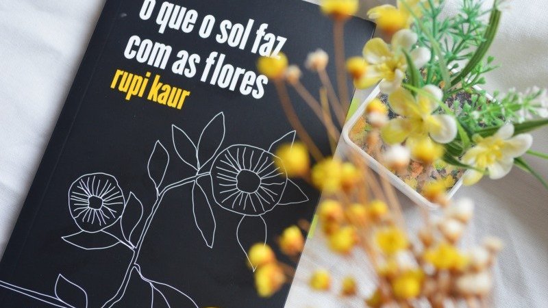 Livro O que o Sol faz com as flore sobre mesa branca, ao lado de arranjo de flores amarelas
